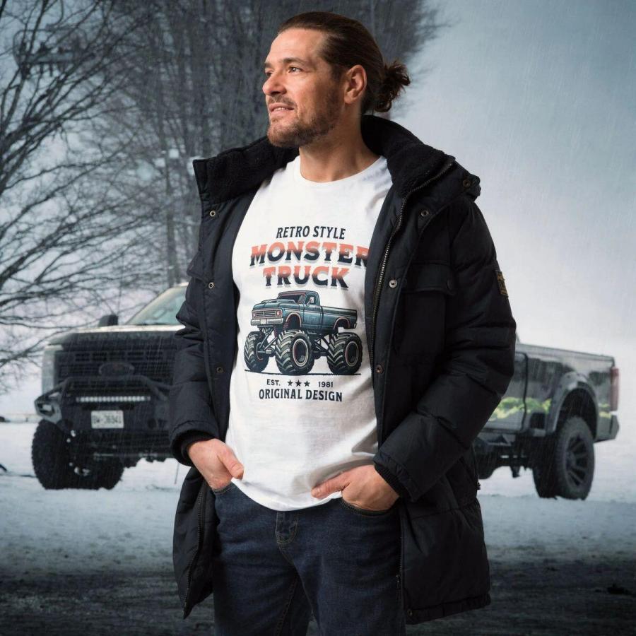 Férfi egy Monster Truck fehér pólóban és kabátban áll egy Bigfoot autó előtt.