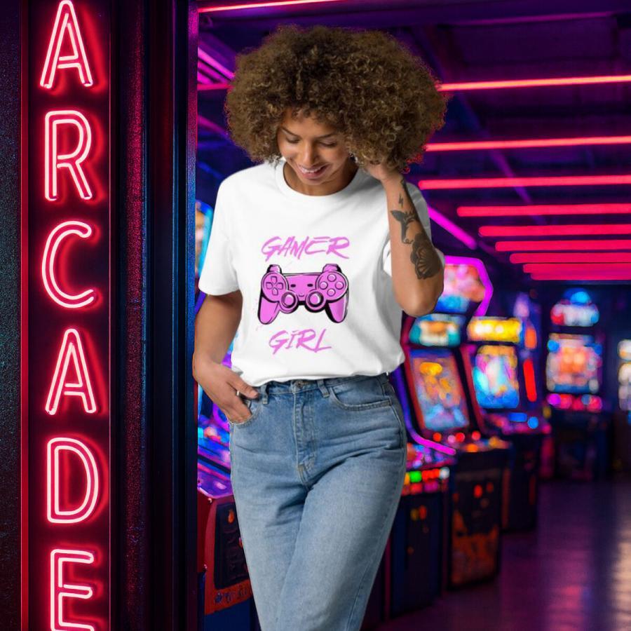 Lány nevetve lép ki egy játékteremből fehér Gamer girl pólóban zsebre tett kézzel.